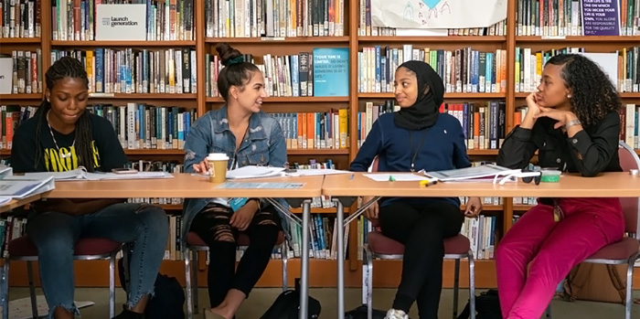Four girls sitting at a desk in a library talking