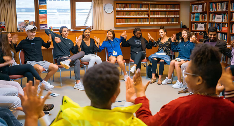 Many kids sitting in a circle and high fiving